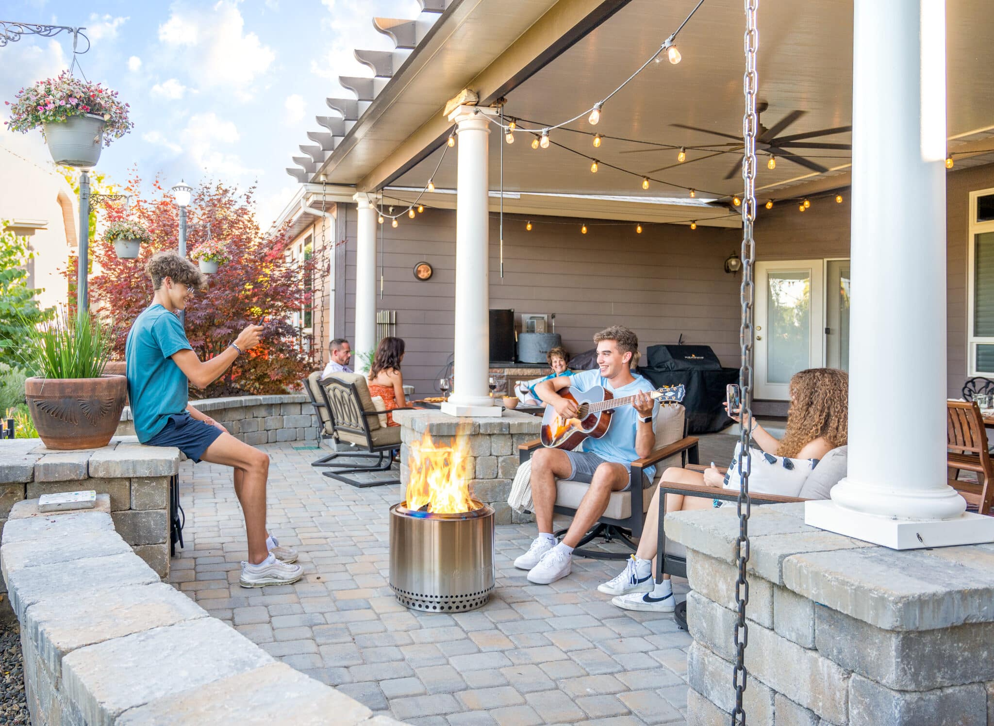 A large family gathered around a fire pit roasting marshmallows under a tan patio cover in Nampa, Idaho.