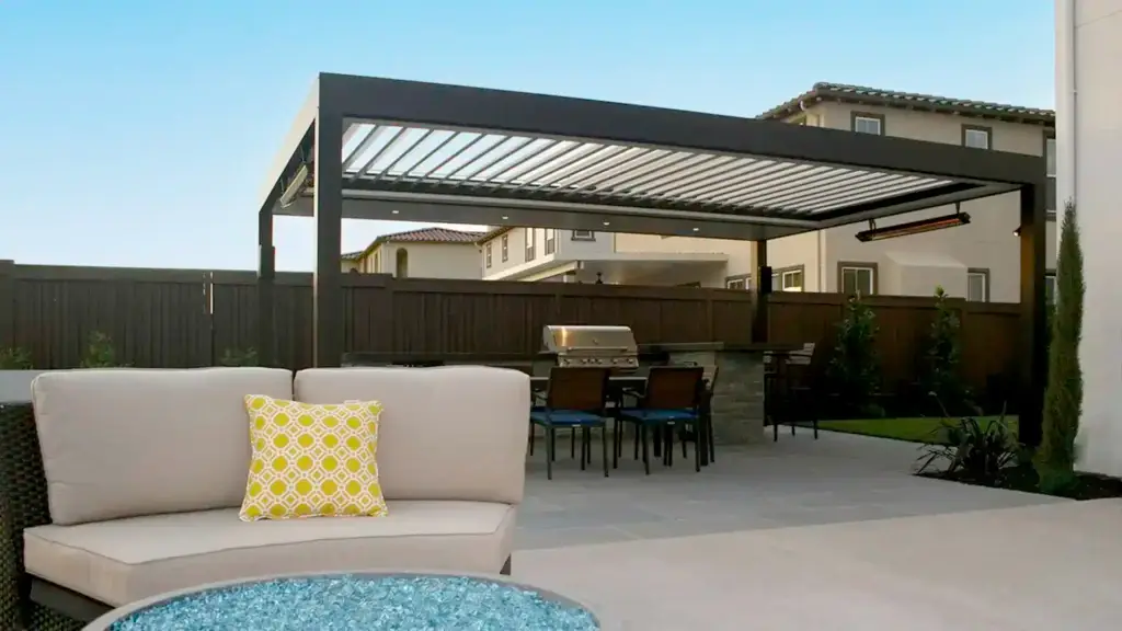 Modern backyard with a black pergola, outdoor dining table, grill, and beige sectional seating with a yellow patterned cushion; pool in the foreground.