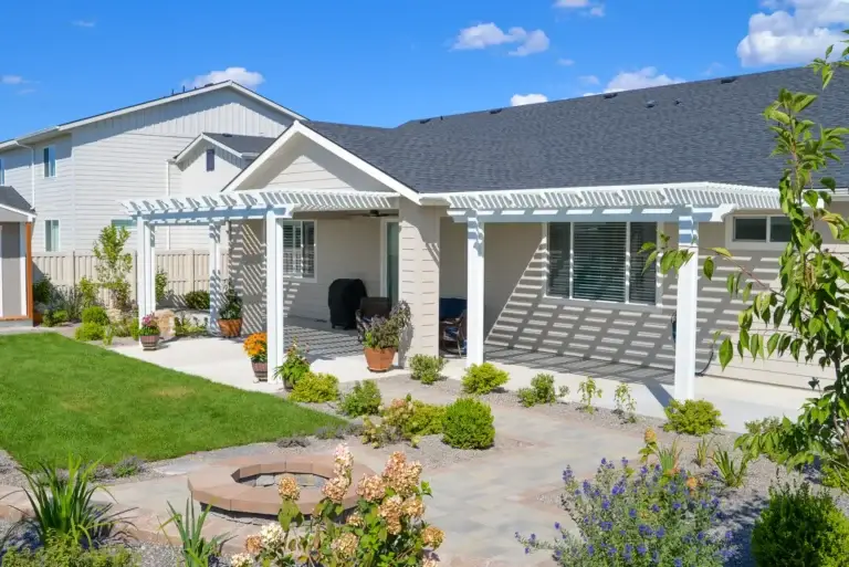White aluminum pergola installed over a landscaped backyard patio