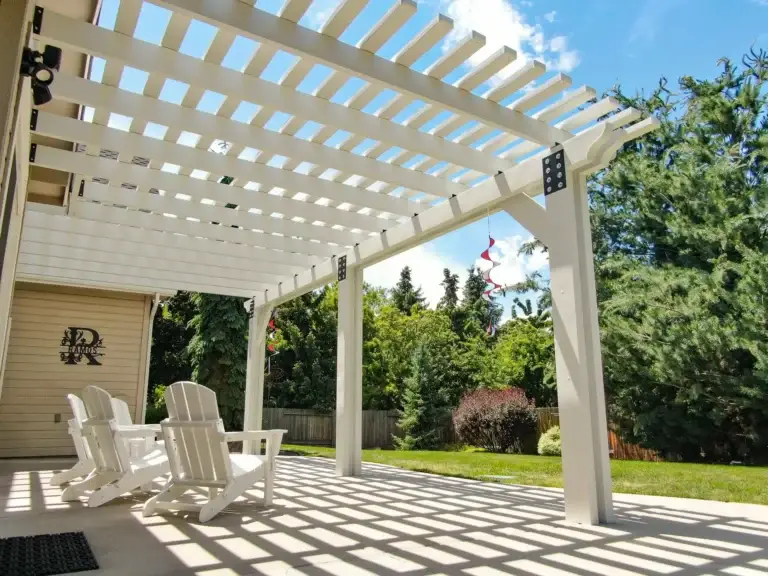 White aluminum pergola creating decorative shade over a backyard patio