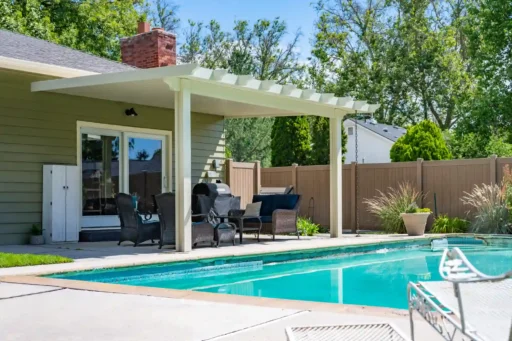 Backyard patio with a white pergola, outdoor seating, and a rectangular pool along a fenced yard.