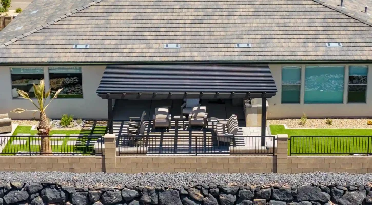 Aerial view of a modern house with a large grey shingle roof, a covered patio with outdoor seating, and a stone seawall in front.