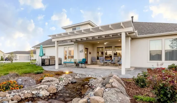 Custom white pergola installed over a Boise backyard patio with outdoor seating, landscaping, and decorative water feature.