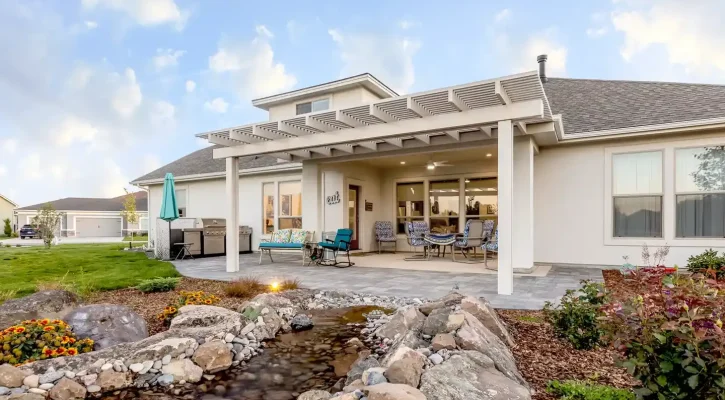 Custom white pergola installed over a Boise backyard patio with outdoor seating, landscaping, and decorative water feature.