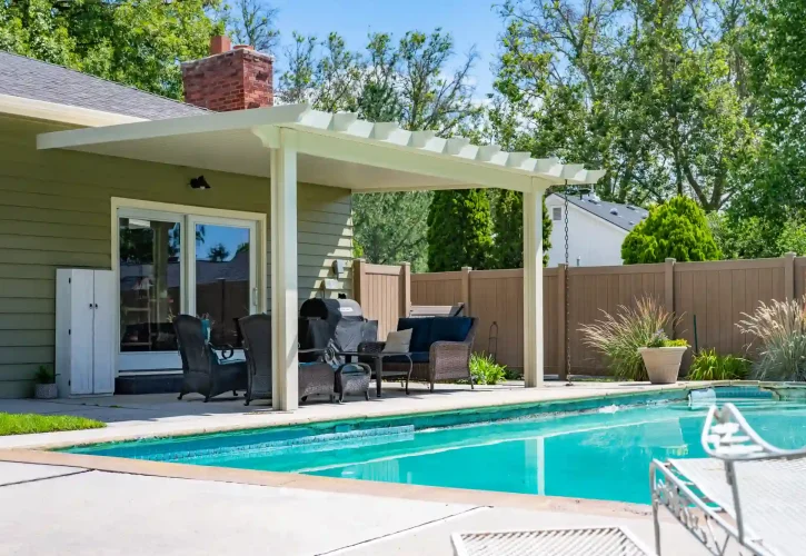 Backyard patio with a white pergola, outdoor seating, and a rectangular pool along a fenced yard.